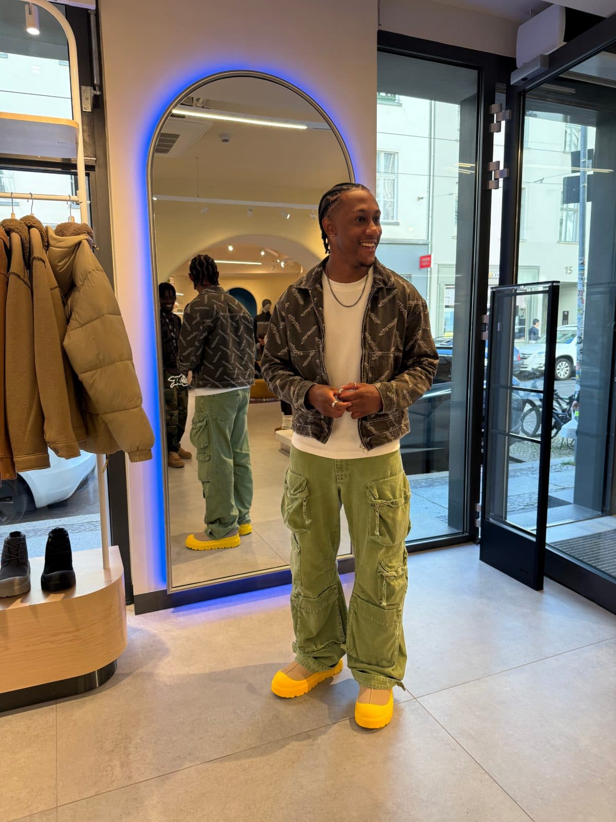 Brandon standing in front of an arched mirror in a Berlin shop, laughing, his back reflected behind him.